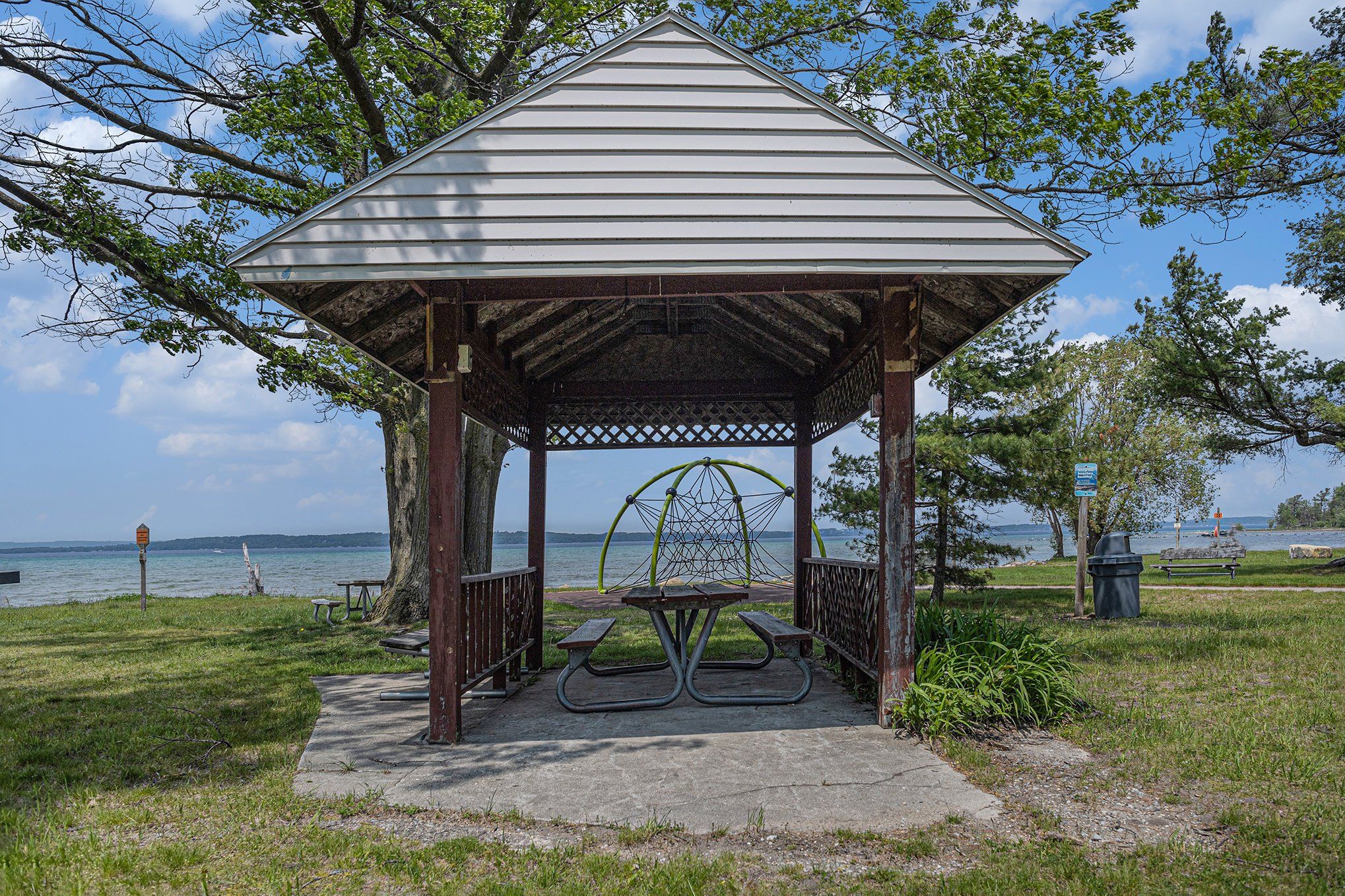 Um gazebo com mesa de piquenique e bancos, com vista para um corpo d'água.
