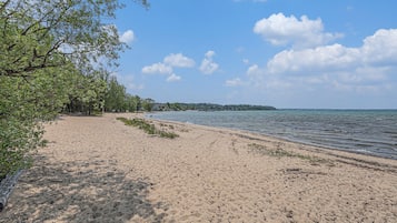 A sandy beach with a calm sea, trees, and a clear sky.