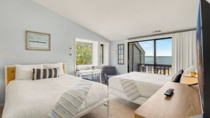 Ein Hotelzimmer mit zwei Betten, einem Schreibtisch, einem Sessel, einem Fernseher und Blick auf den Strand.