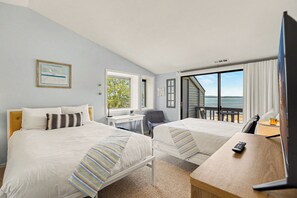 Ett hotellrum med två sängar, ett skrivbord, en stol, en TV och utsikt över stranden.