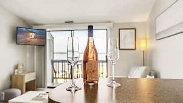 A bar area with a bottle of champagne and two glasses on a counter, a television screen in the background, and a view of the sea through large windows.