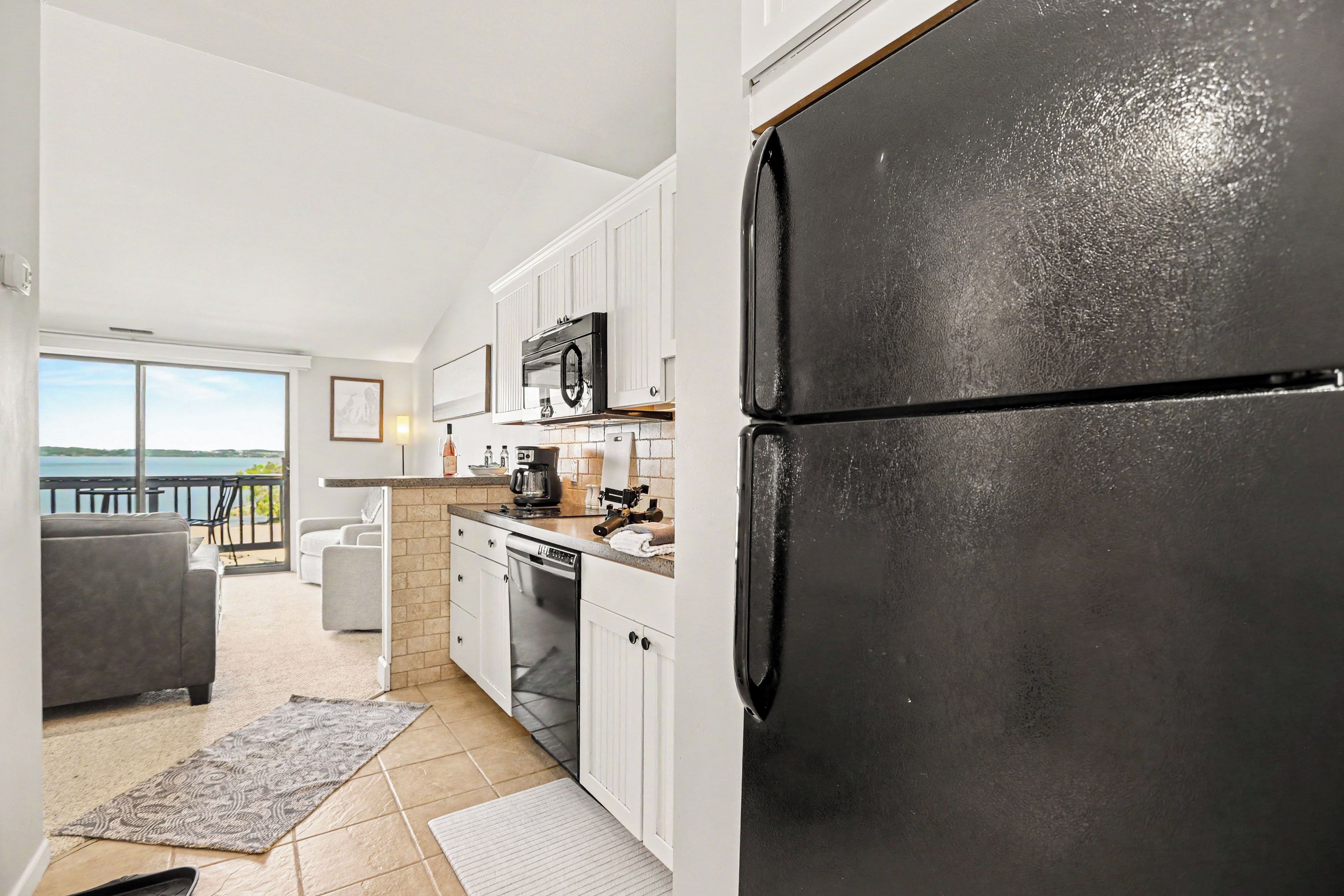 A modern kitchen with white cabinets, a black refrigerator, and a view of the outdoors.