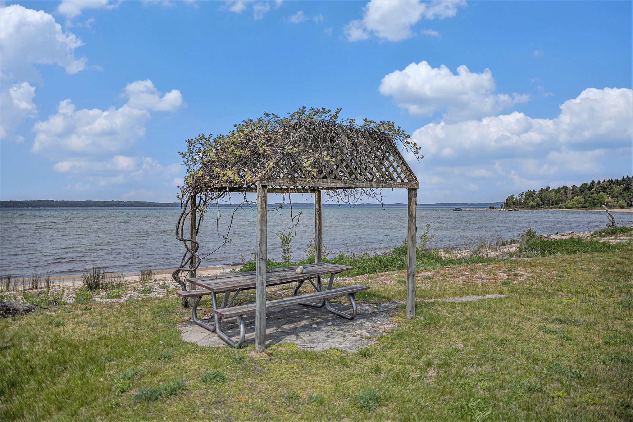 A wooden gazebo with a lattice roof and picnic table by a lake.