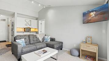 A modern living room with a grey sectional sofa, a white coffee table, and a mounted TV displaying 'True North Property Management'.