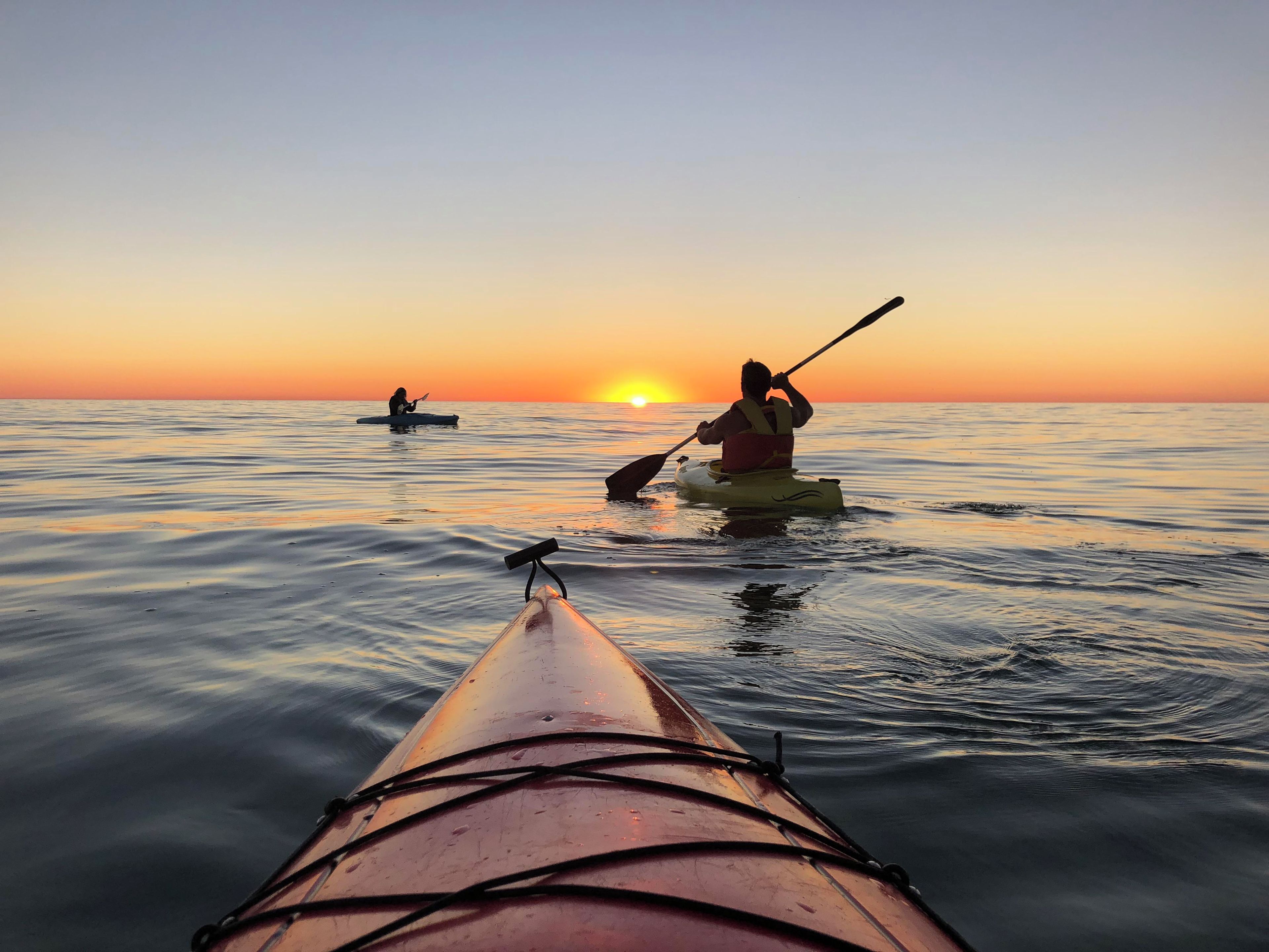 A kayak on calm water with a sunset in the background.