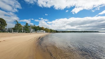 A beach with a sandy shore, a calm body of water, and a clear sky with clouds.