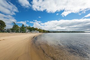 Una playa con orilla arenosa, aguas tranquilas y cielo despejado con nubes.