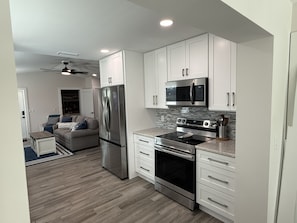 A modern kitchen with white cabinets, stainless steel appliances, and a herringbone wood floor. - New Construction.  Sunny Escape Near Anna Maria : 3BR/2BA Home with Resort Pool! (Bradenton)