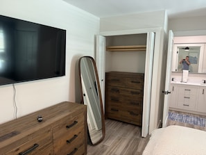 A bedroom with a wooden dresser, a TV, a wardrobe, and a mirror. - New Construction.  Sunny Escape Near Anna Maria : 3BR/2BA Home with Resort Pool! (Bradenton)