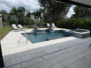 Une piscine rectangulaire dotée d’un jacuzzi intégré, entourée d’une terrasse carrelée avec des chaises longues.