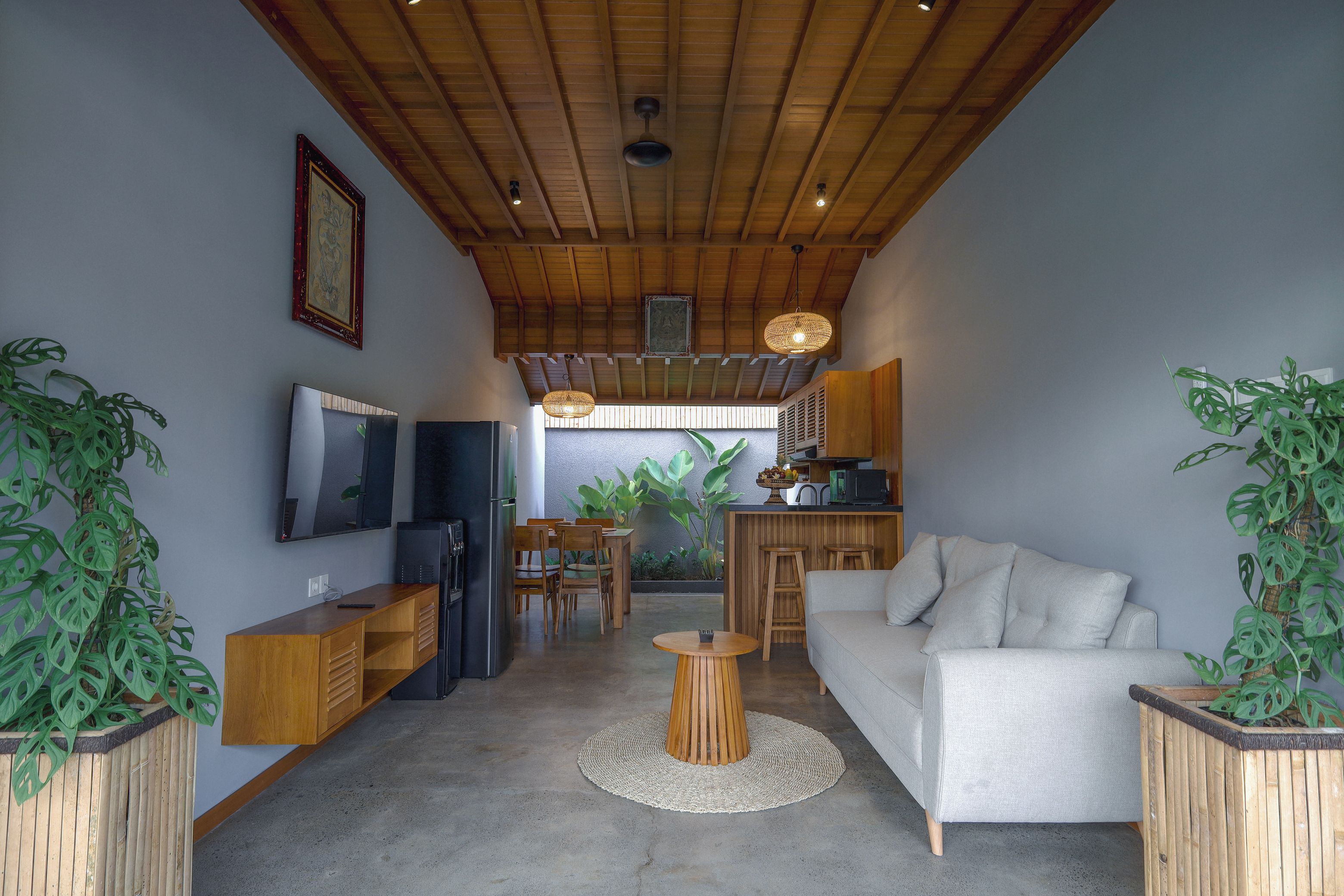 Un espacio habitable moderno con techo alto, vigas de madera, televisor de pantalla plana, sofá, zona de comedor y plantas en macetas.