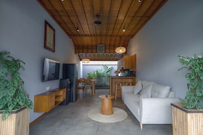 Un soggiorno moderno con soffitto alto, travi in legno, televisione a schermo piatto, un divano, un'area pranzo e piante in vaso.
