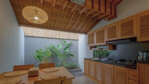 A modern kitchen with wooden cabinets, a built-in stove, and a dining area with a table and chairs. - D TEBA Villas (Badung)