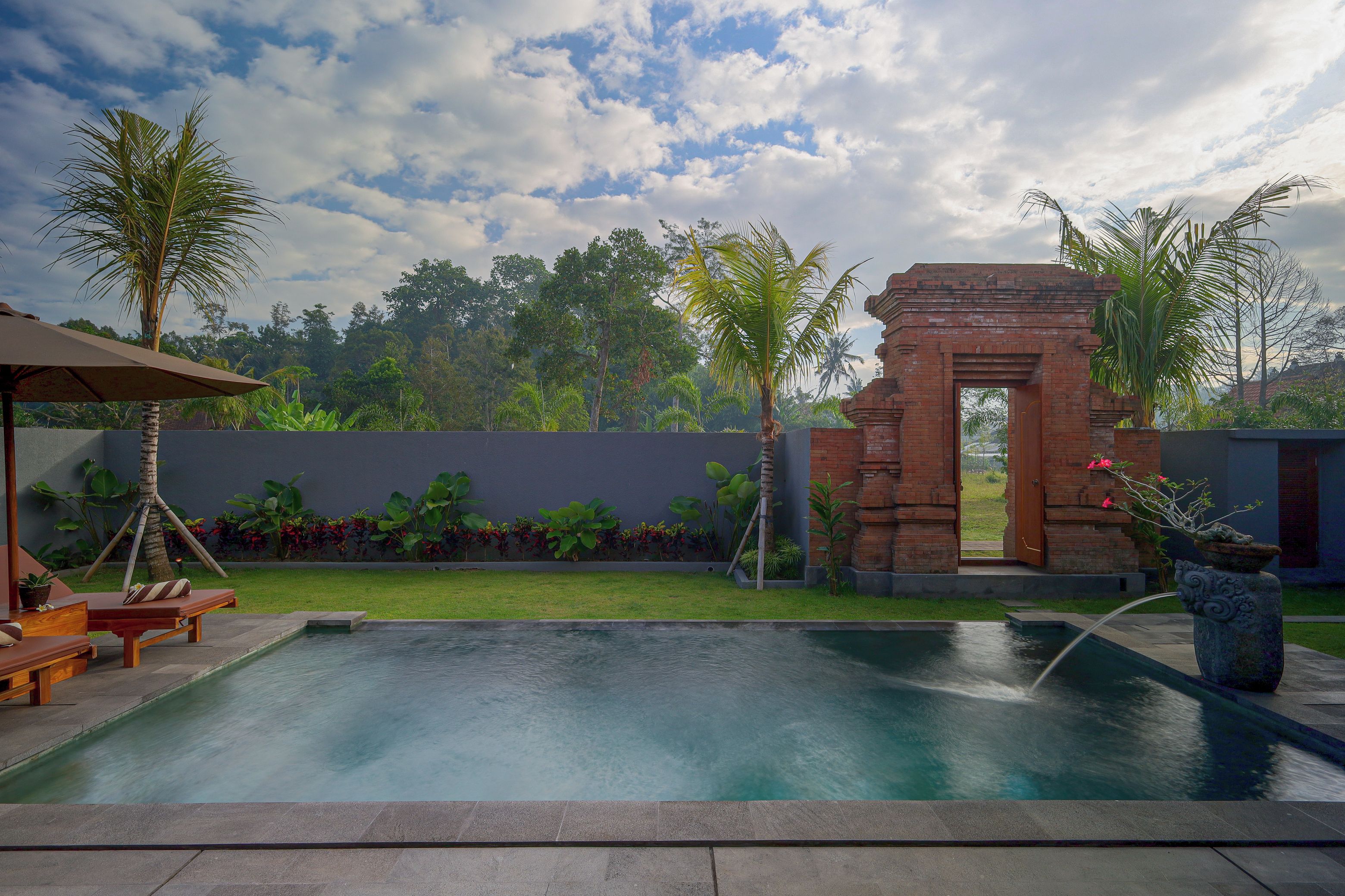 Una piscina con una estructura de ladrillo y palmeras al fondo.
