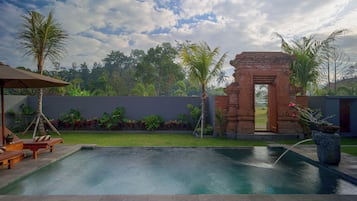 Una piscina con una estructura de ladrillo y palmeras al fondo.