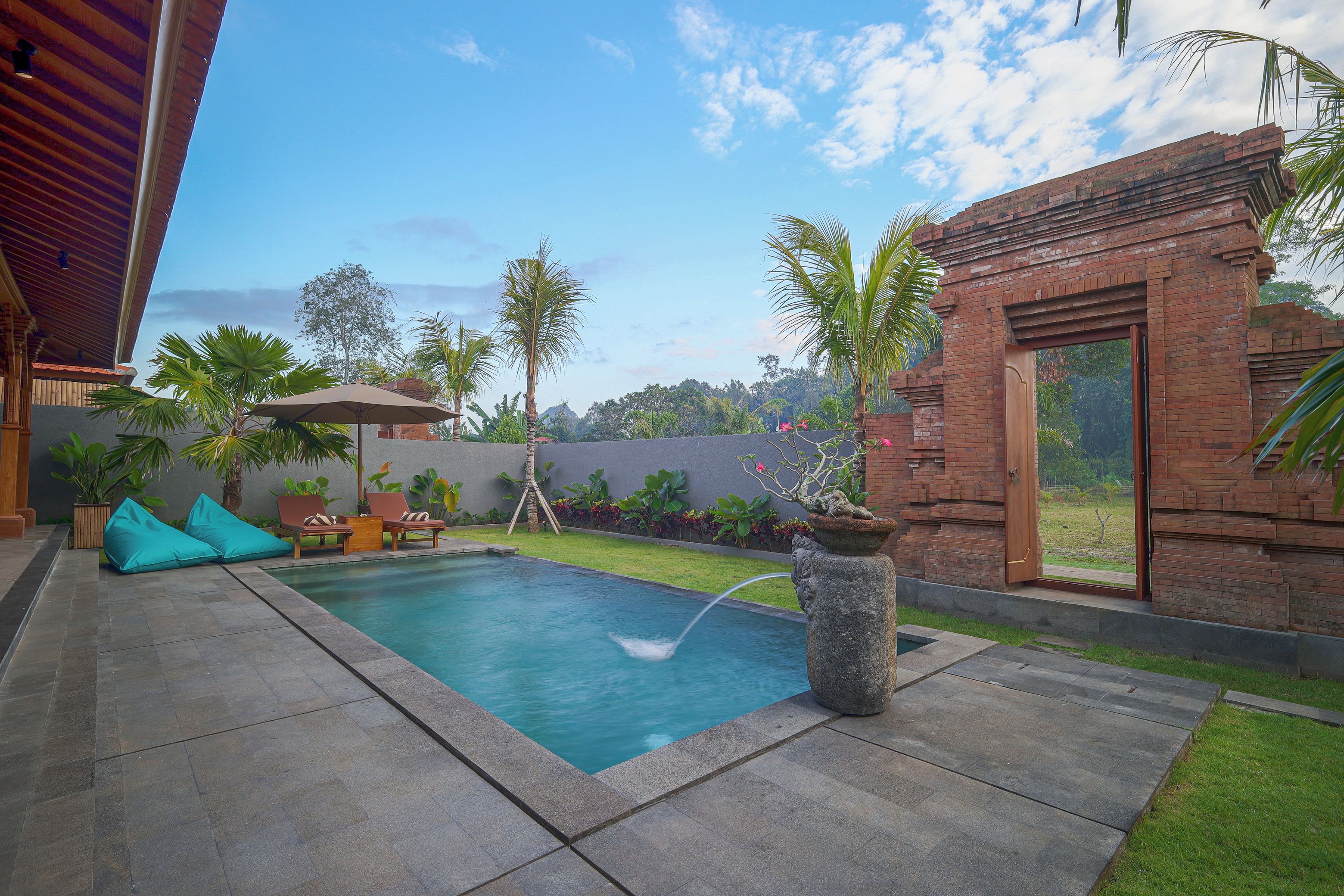 A swimming pool with a water feature, surrounded by a patio with lounge chairs and a covered seating area.