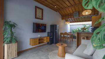 Un soggiorno moderno con soffitto in legno, TV a schermo piatto, frigorifero, angolo pranzo con sedie di legno e piante in vaso.