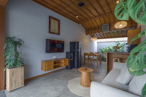 Un soggiorno moderno con soffitto in legno, TV a schermo piatto, frigorifero, angolo pranzo con sedie di legno e piante in vaso.