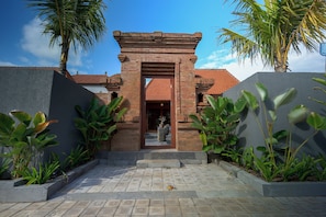 Un ingresso di un edificio con facciata in mattoni, tetto a tegole visibile attraverso la porta e un vialetto lastricato che conduce all'ingresso.