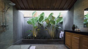 A modern bathroom with a shower, a sink, and a large mirror. There are plants and a wooden bench. - D TEBA Villas (Badung)