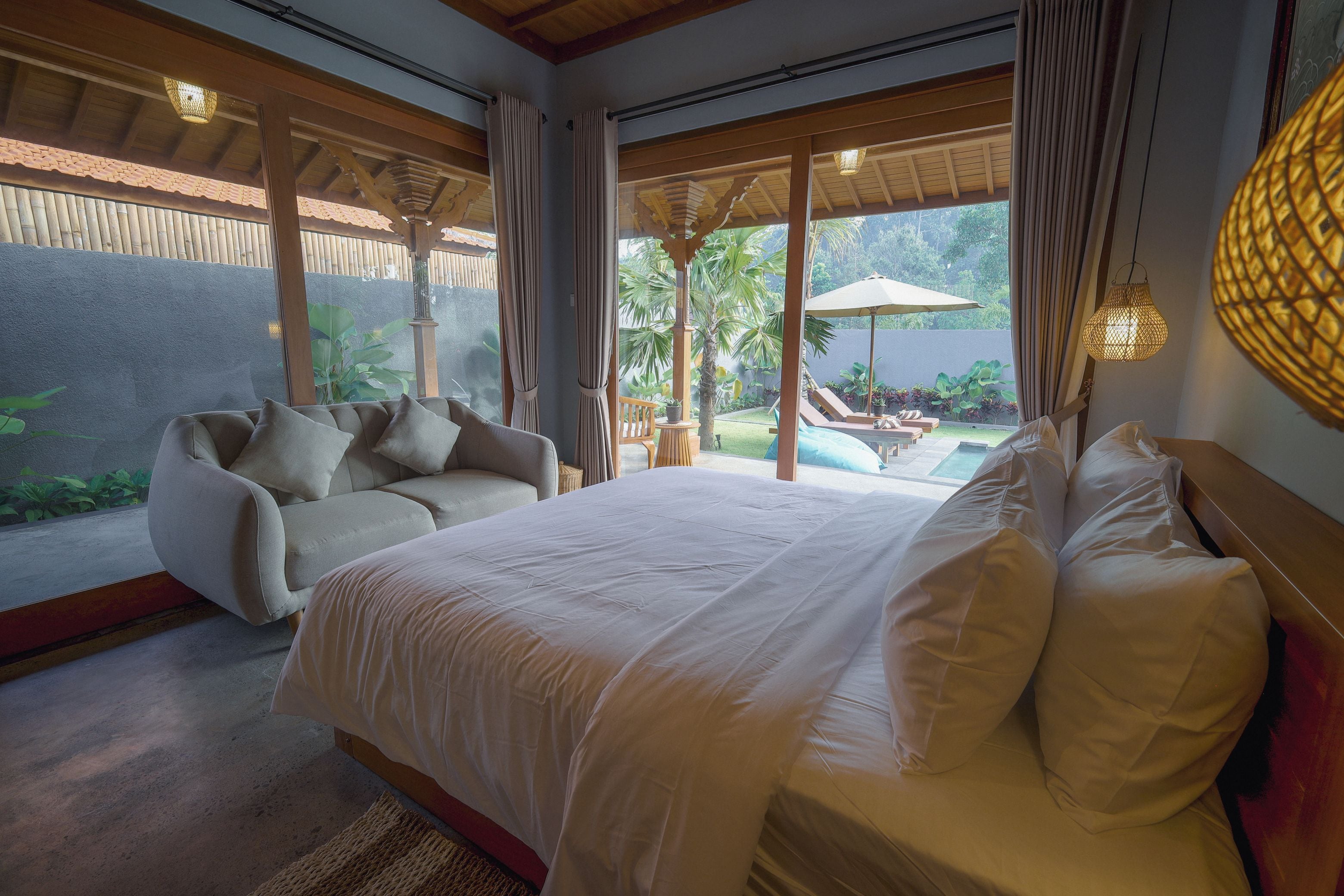 Ein Schlafzimmer mit einem großen Bett, einem Sofa und Blick auf Pool und Garten.