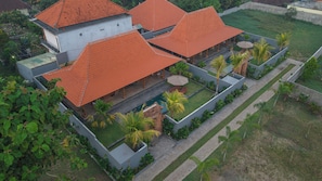Un edificio de varios pisos con techo de tejas rojas, piscina y un jardín bien cuidado con palmeras.