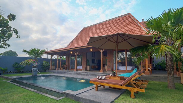 A poolside area with lounge chairs, a covered seating area, and a building with a tiled roof. - D TEBA Villas (Badung)