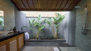 A modern bathroom with a black sink, wooden cabinets, a shower, and large green plants. - D TEBA Villas (Badung)