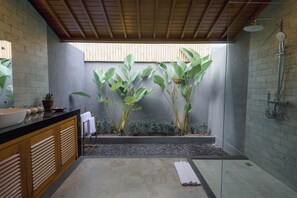 Un baño moderno con un lavamanos negro, armarios de madera, ducha y plantas verdes grandes.