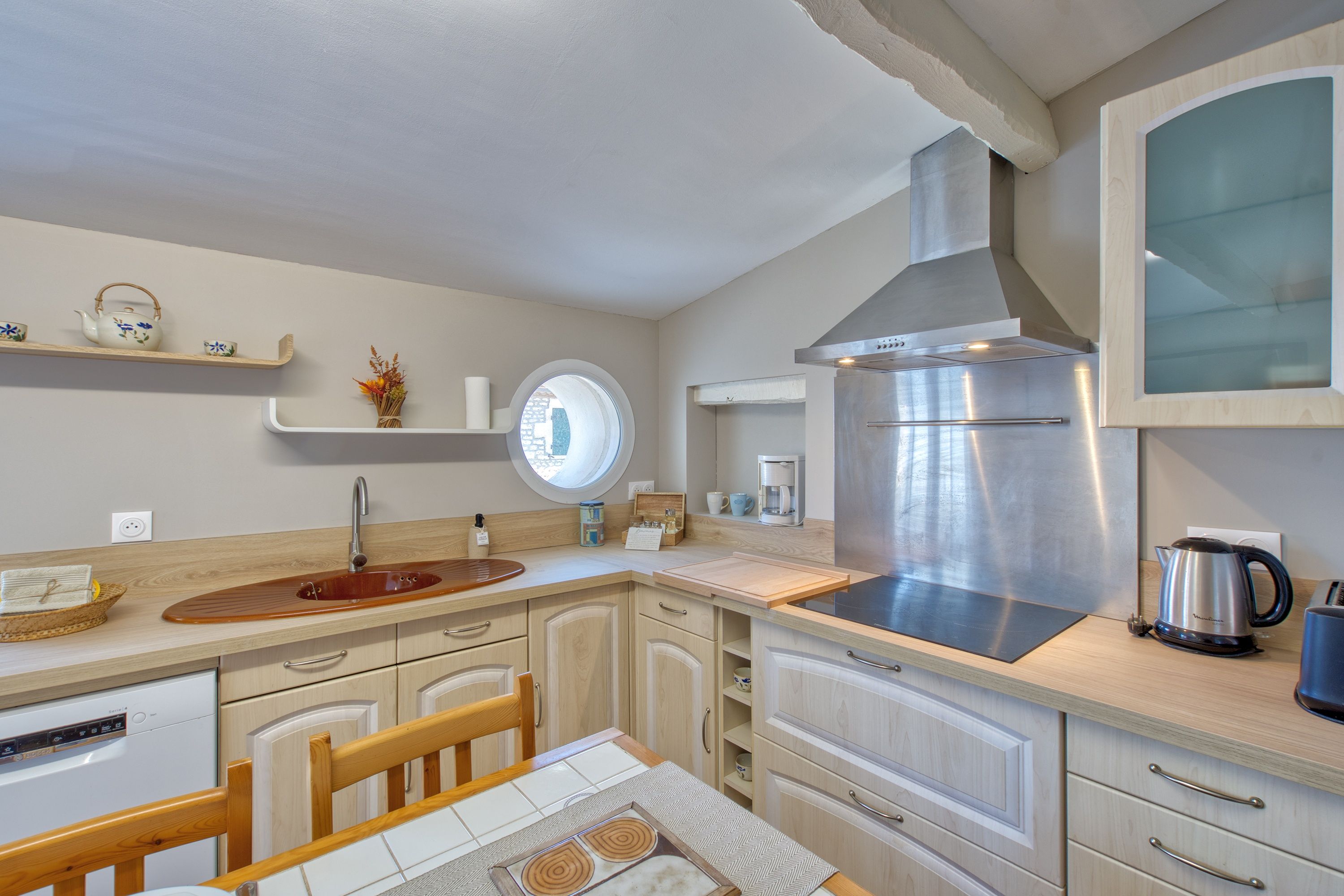Une cuisine moderne dotée d’une hotte en acier inoxydable, de meubles en bois et d’une fenêtre ronde.