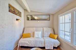 A room with a white textured wall, a large window with white frames, a white sofa with two yellow pillows, and a mirror above the sofa. - L’Écrin de l’Estuaire - 1km de la Plage (Meschers-sur-Gironde)