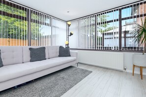 Una sala de estar moderna con un sofá blanco, cojines grises, un tapete gris y una lámpara de pie.