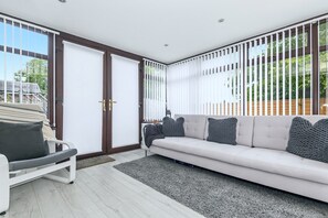 A modern living room with a sofa, a chair, and a large window with blinds. - Maison Modern - Family-Friendly with Lovely Garden - Pass the Keys (Leeds)