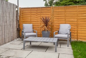 A patio with two grey chairs and a table, a wooden fence, and a potted plant. - Maison Modern - Family-Friendly with Lovely Garden - Pass the Keys (Leeds)