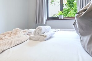 Una cama bien hecha con toallas blancas dobladas y un edredón blanco mullido.