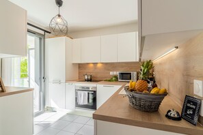 A modern kitchen with white cabinetry, a wooden countertop, a microwave, an oven, and a fruit basket. - La Citadelle - à 500 m de la télécabine du Prorel (Briancon)