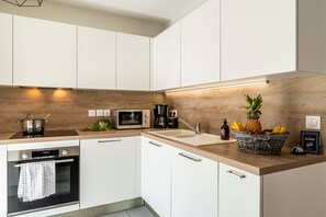 A modern kitchen with white cabinets, a microwave, a coffee maker, and a fruit basket. - La Citadelle - à 500 m de la télécabine du Prorel (Briancon)