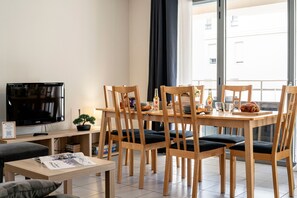 A modern living room with a flat-screen TV, wooden dining table, and chairs. - La Citadelle - à 500 m de la télécabine du Prorel (Briancon)