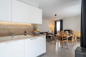 A modern kitchen with white cabinets, a wooden countertop, and a dining area with a table and chairs. - La Citadelle - à 500 m de la télécabine du Prorel (Briancon)