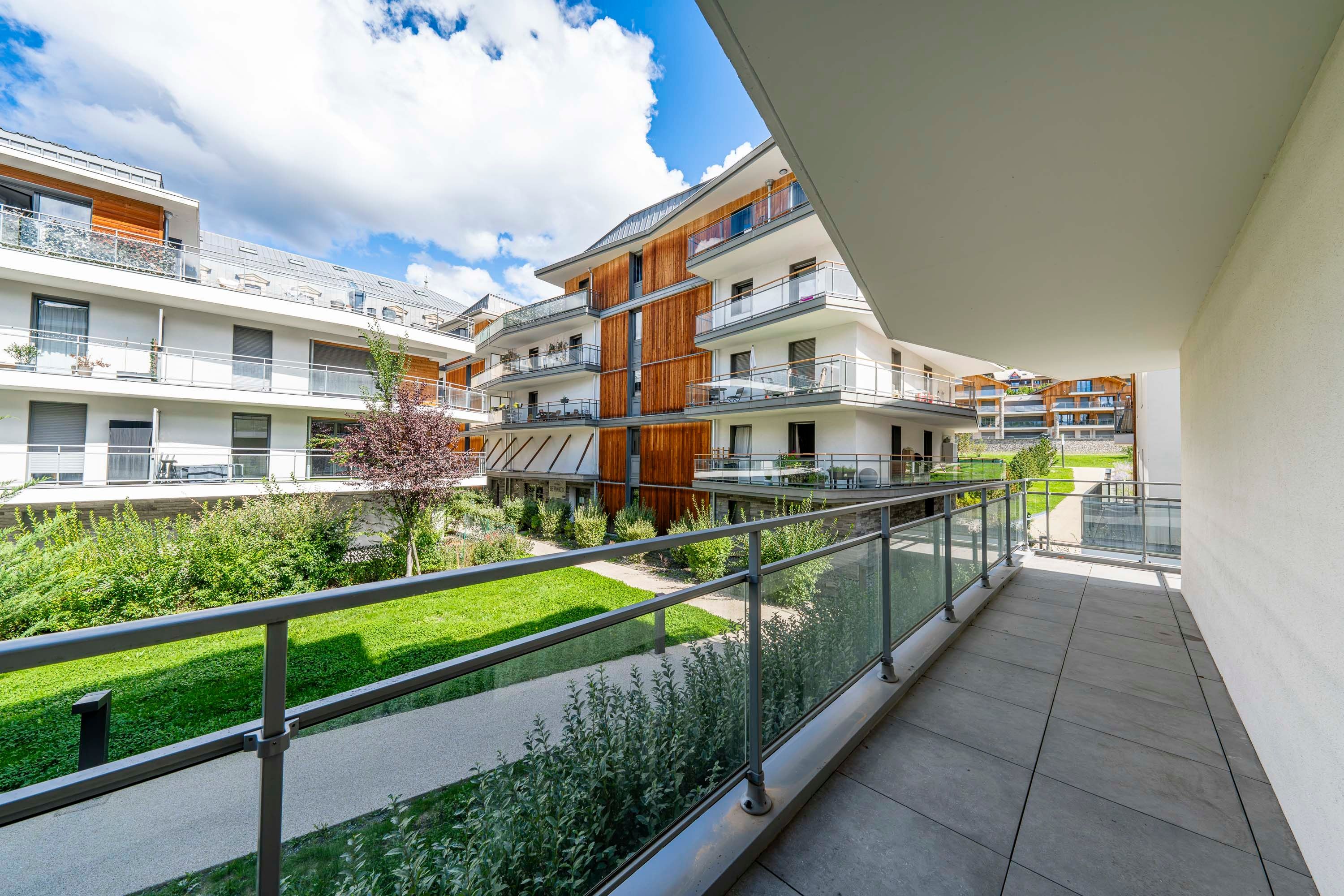 A modern apartment building with multiple balconies, a glass railing, and a well-maintained garden area.