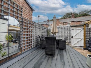 Een terras met een tafel en stoelen, omgeven door een houten omheining en een bakstenen muur.