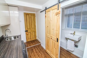 A kitchen with a stainless steel sink, wooden flooring, a sliding wooden door, and a window with blinds. - The Seaside Family Retreat - Pass the Keys (Whitley Bay)