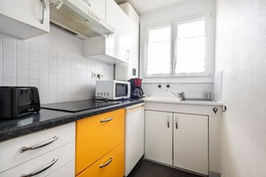 Et køkken med hvide skabe, en gul skuffe, en sort brødrister, en hvid mikrobølgeovn og et vindue med gardiner.