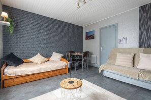 A modern living room with a brick wall, a wooden sofa, a beige sofa, a dining table with chairs, and a hanging light fixture. - Le Studio des Oyats - à 400 m de la plage (Berck)