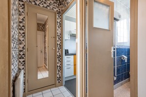 A hallway with patterned walls leading to a kitchen area with blue tiles. - Le Studio des Oyats - à 400 m de la plage (Berck)