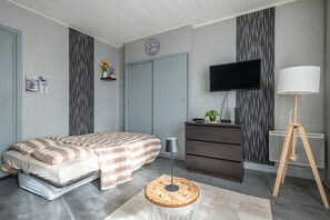 A bedroom with a bed, dresser, TV, lamp, and a small table with a plant. - Le Studio des Oyats - à 400 m de la plage (Berck)