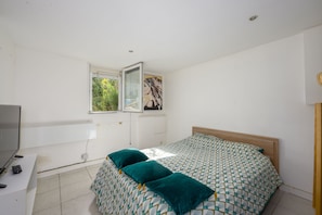 Une chambre à coucher comprenant un lit, un bureau, une télévision et une fenêtre donnant sur un espace verdoyant.