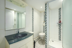 A bathroom with a glass sink, white toilet, and a shower with mosaic tiles.