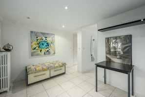 A modern interior with a white tiled floor, a bench with patterned cushions, a table, and two wall-mounted artworks.