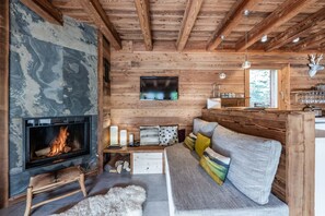 A cozy cabin interior with a fireplace, wooden walls, a sofa with colorful cushions, and a mounted television.